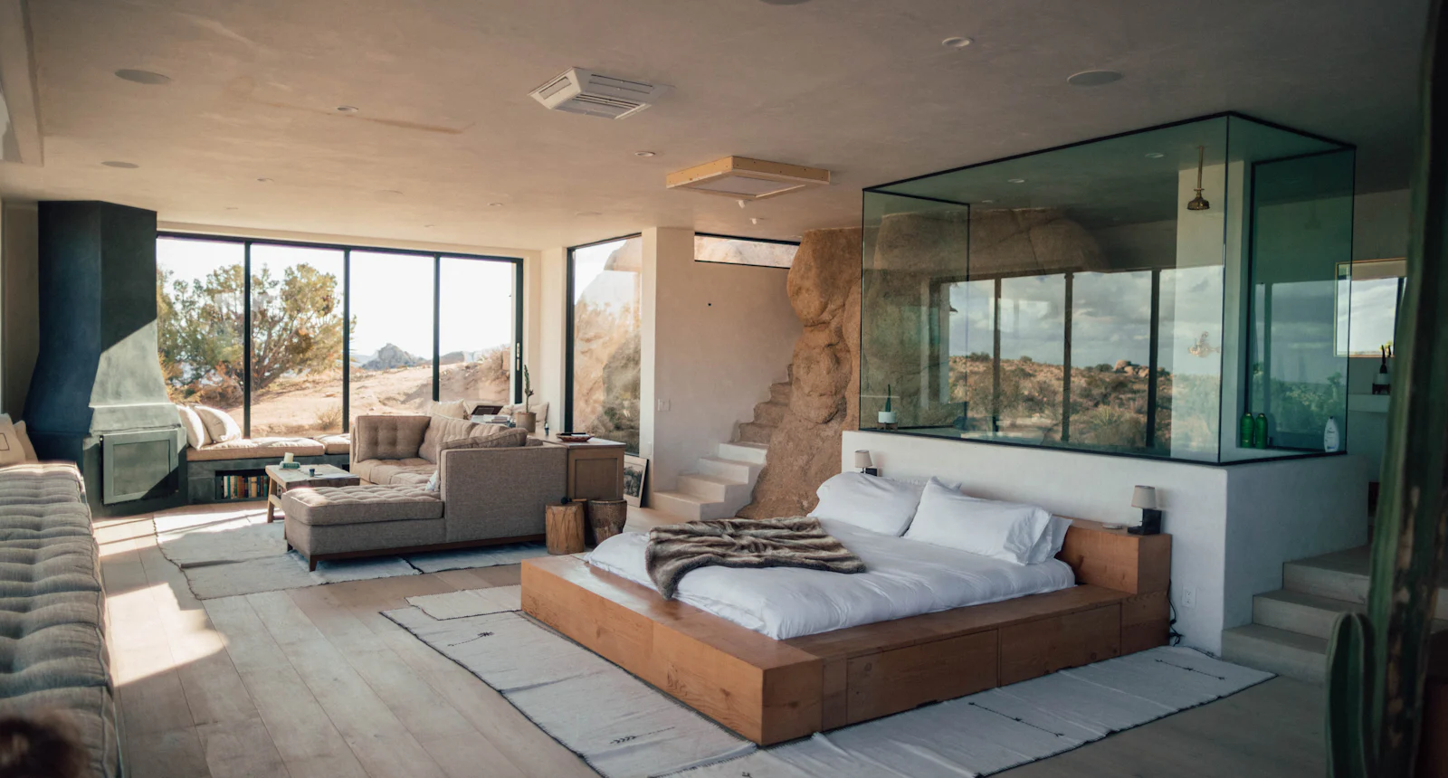 Suíte envidraçada no deserto, com cama de madeira, sofá e vista para as rochas