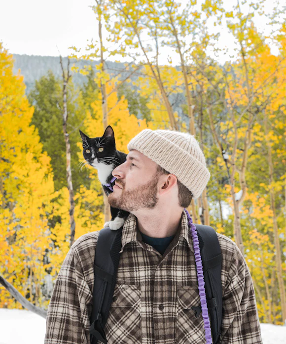 Homem caminhando com um gato preto e branco no ombro
