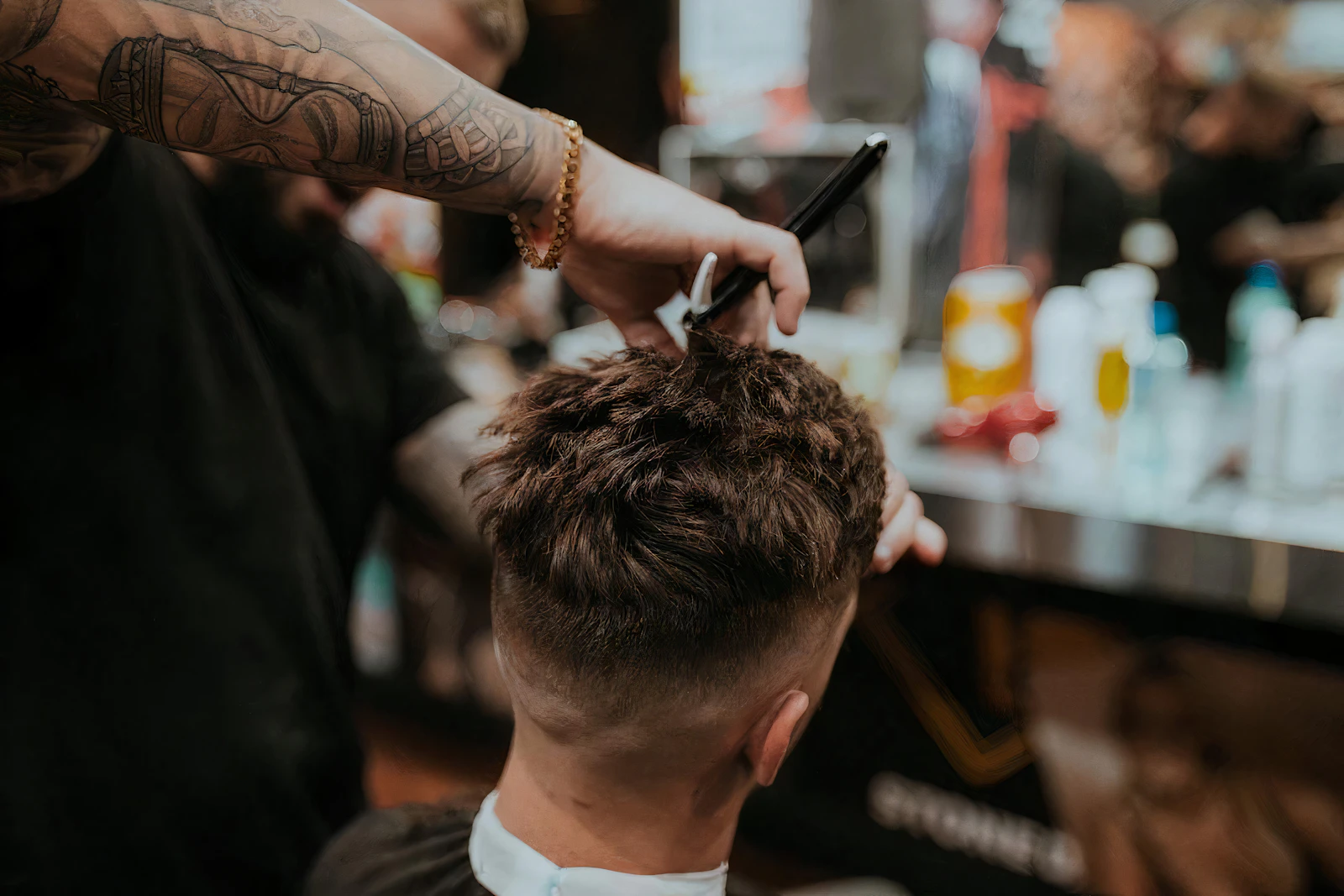 Barbeiro de braço tatuado finalizando um degradê com navalha, dentro da barbearia