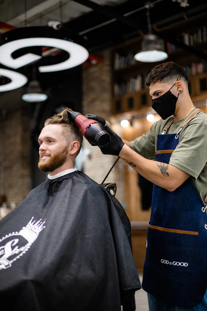 Barbeiro secando o cabelo de um cliente barbudo com secador
